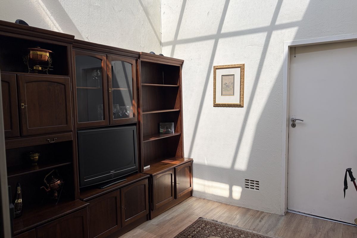 A living area featuring laminate flooring and high ceilings with natural light streaming through a skylight or high window.