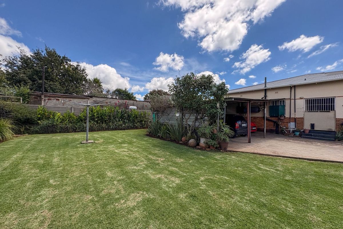 Spacious rear garden featuring a well-maintained lawn, perimeter walling, and a covered carport area attached to the main house structure.