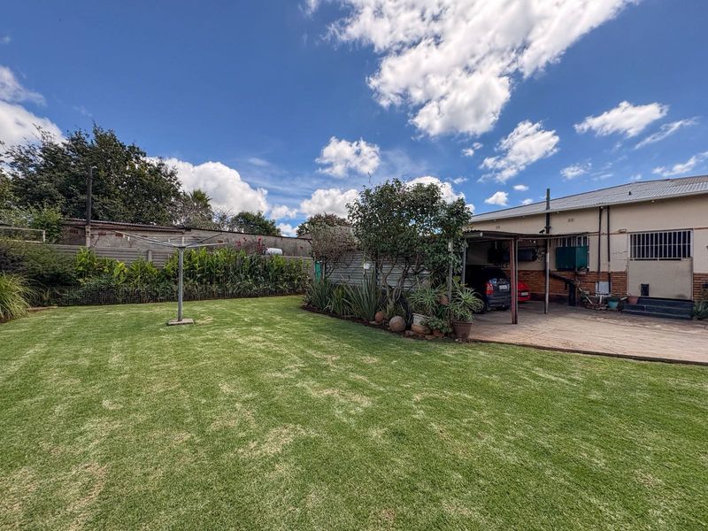Spacious rear garden featuring a well-maintained lawn, perimeter walling, and a covered carport area attached to the main house structure.