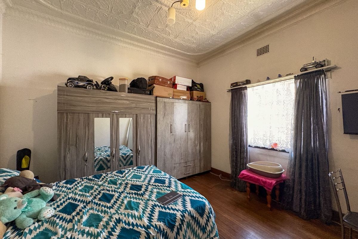 A bedroom featuring original pressed metal ceilings, a decorative ceiling rose, timber flooring, and built-in wardrobe storage.