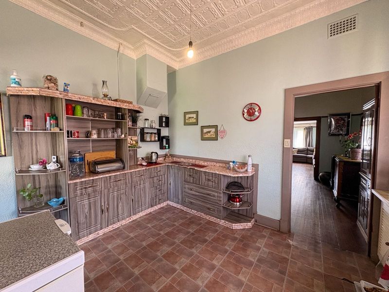 A dated kitchen featuring laminate cabinetry, tiled flooring, and a distinctive ornate pressed metal ceiling, offering potential for a modern renovation.