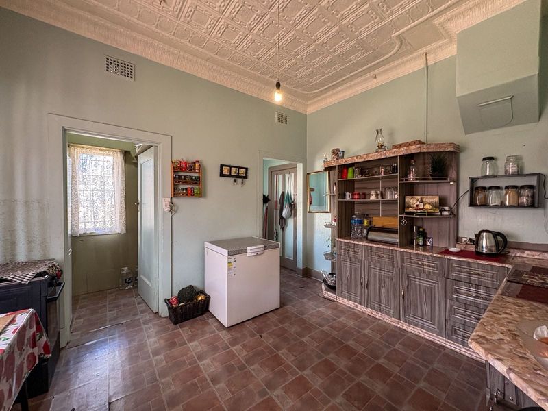 A dated kitchen featuring original pressed metal ceilings, tiled flooring, and built-in cabinetry, offering significant potential for a modern renovation.