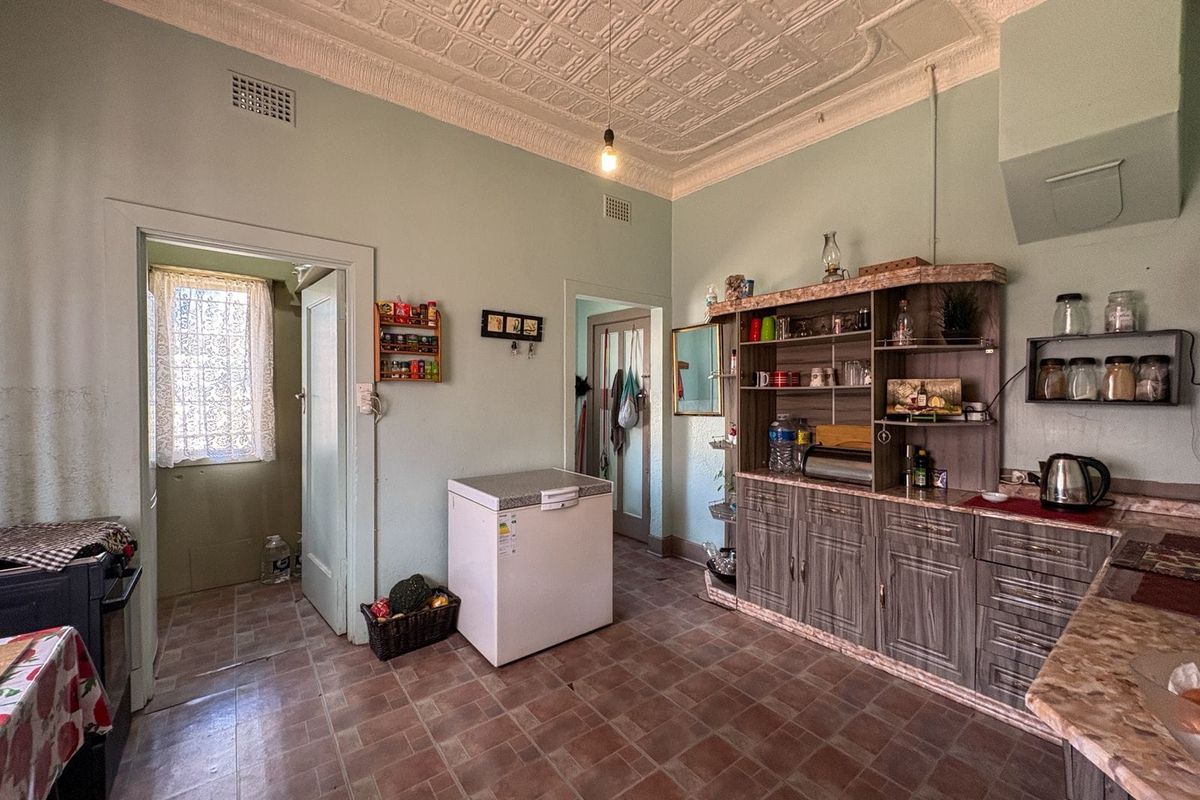 A dated kitchen featuring original pressed metal ceilings, tiled flooring, and built-in cabinetry, offering significant potential for a modern renovation.