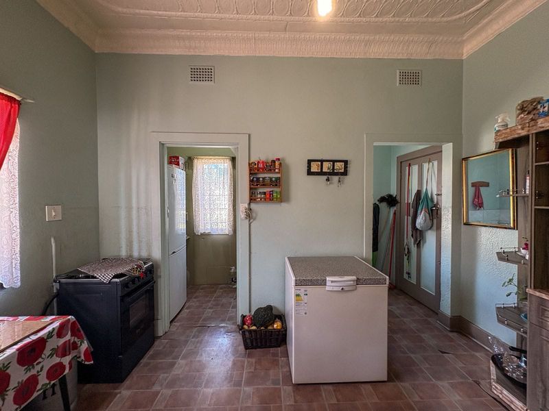 A dated kitchen area featuring an ornate plaster ceiling, tiled flooring, and a freestanding oven, with access to an adjacent utility space.
