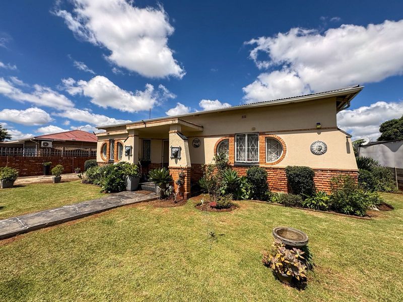 A well-maintained single-story house featuring a brick and plaster facade, arched windows with security bars, and a neat front garden with a concrete walkway.