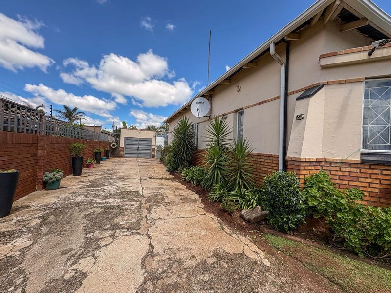 Side view of the property featuring a long concrete driveway, brick boundary wall, and established garden beds along the house exterior.