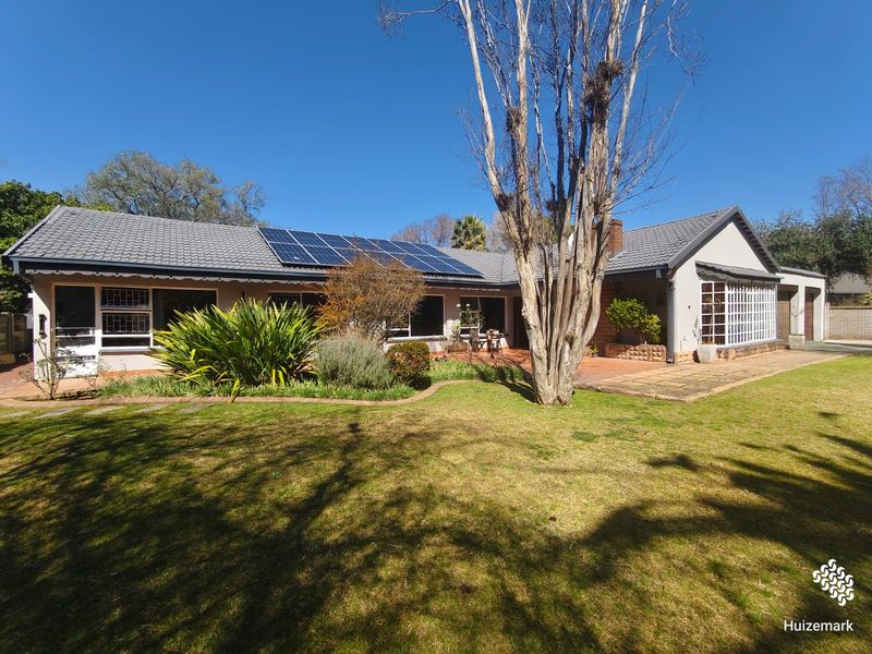 Rear view of the house featuring a paved patio area, established garden, and roof-mounted solar panels under a clear blue sky.
