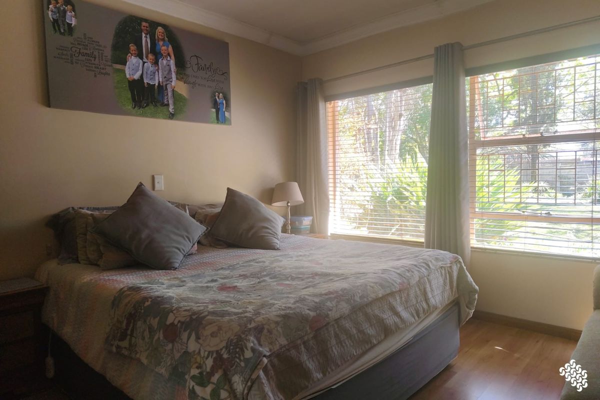 A well-lit bedroom featuring laminate flooring, recessed downlighting, and large windows fitted with security bars and venetian blinds.
