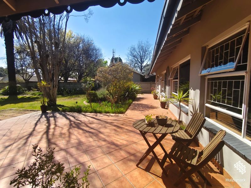 A spacious tiled patio area overlooking a well-maintained garden, featuring security bars on the windows and a covered awning.
