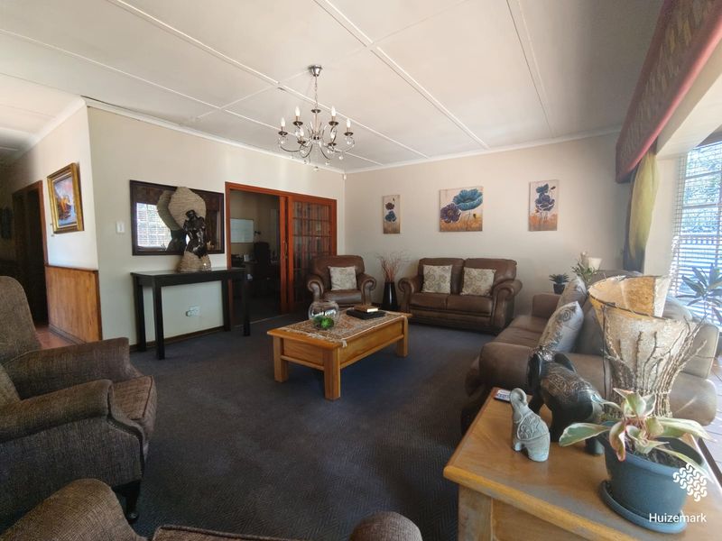 Spacious living room featuring a panelled ceiling, central chandelier, and sliding wooden doors leading to an adjacent room, finished with carpeted flooring.