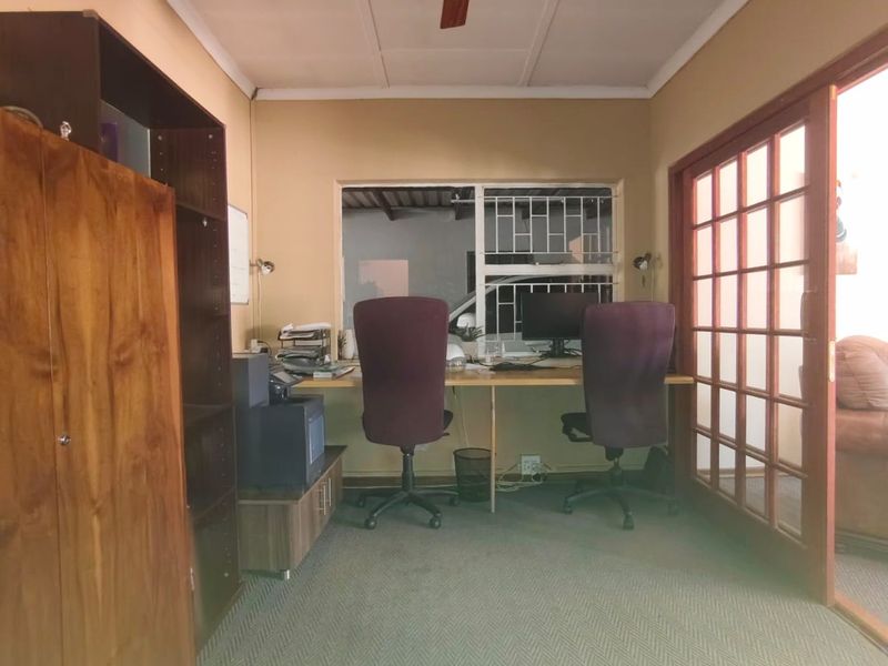 A functional home office space featuring a ceiling fan, carpeted flooring, and glass-paneled french doors providing natural light and access.