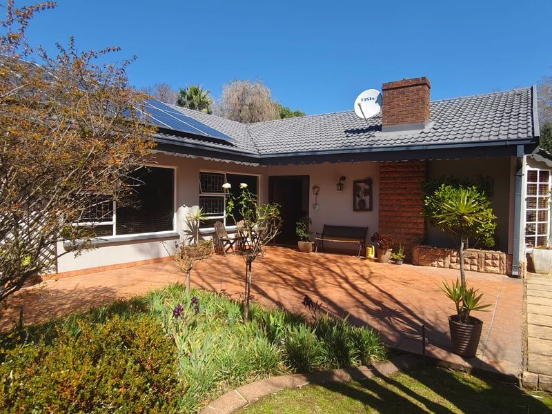 A well-maintained rear exterior featuring a spacious tiled patio, brick chimney, and solar panels, overlooking a landscaped garden area.