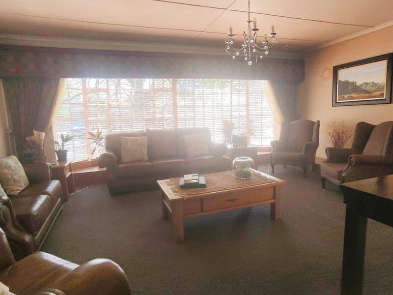 Spacious living room featuring a large bay window, carpeted flooring, and a central chandelier, offering a comfortable and traditional living space.