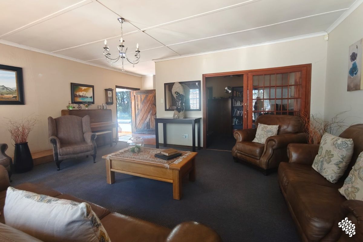 Spacious living room featuring a chandelier, carpeted flooring, and a sliding glass door leading to an adjacent room.