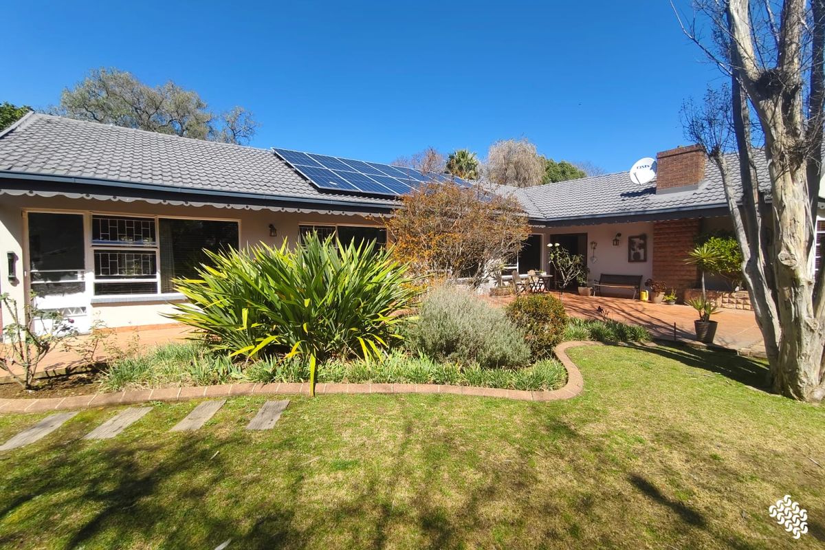 Rear view of the house featuring a paved patio, landscaped garden, and roof-mounted solar panels under a clear blue sky.