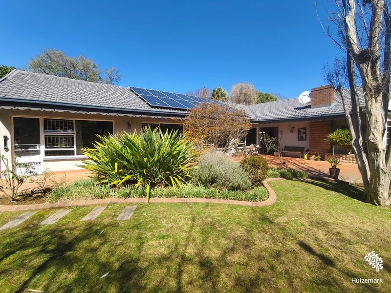 Rear view of the house featuring a paved patio, landscaped garden, and roof-mounted solar panels under a clear blue sky.