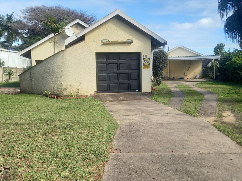 Front view of the property featuring a single garage, concrete driveway, and an attached carport, set on a grassed lot.