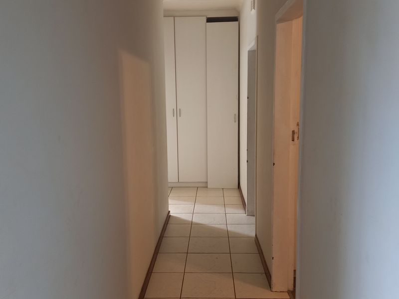A clean, functional hallway featuring neutral tiled flooring and built-in storage cupboards, providing a bright and practical transition space within the home.