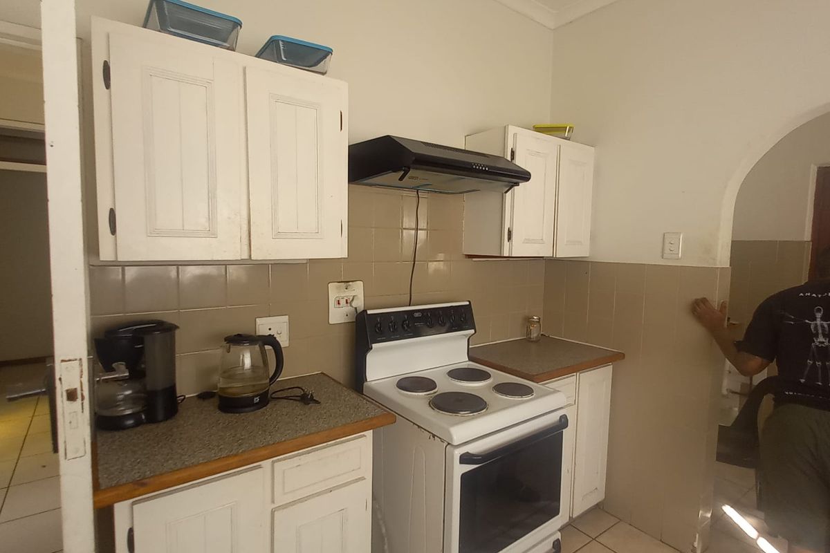 A compact kitchen featuring white cabinetry, a freestanding electric stove with extractor fan, tiled backsplash, and tiled flooring.