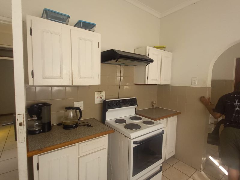 A compact kitchen featuring white cabinetry, a freestanding electric stove with extractor fan, tiled backsplash, and tiled flooring.
