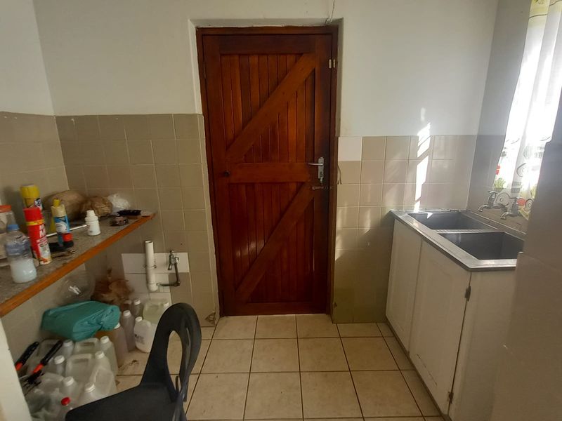 A functional laundry area featuring a double basin sink, tiled splashback, ceramic flooring, and a solid timber door with direct access.