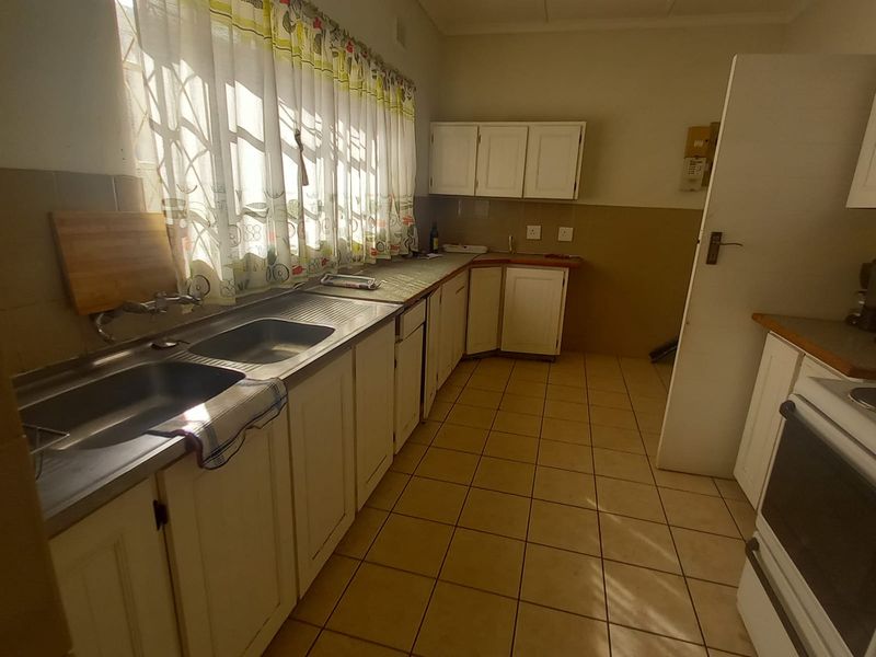 A functional kitchen featuring tiled flooring, a double stainless steel sink, and built-in cabinetry with a tiled splashback.