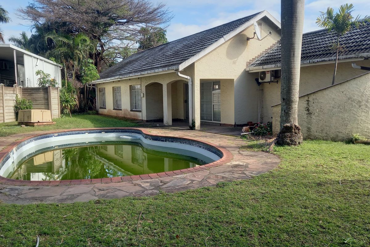 Rear view of the property featuring a swimming pool, paved surround, and a tiled roof structure with exterior wall access.