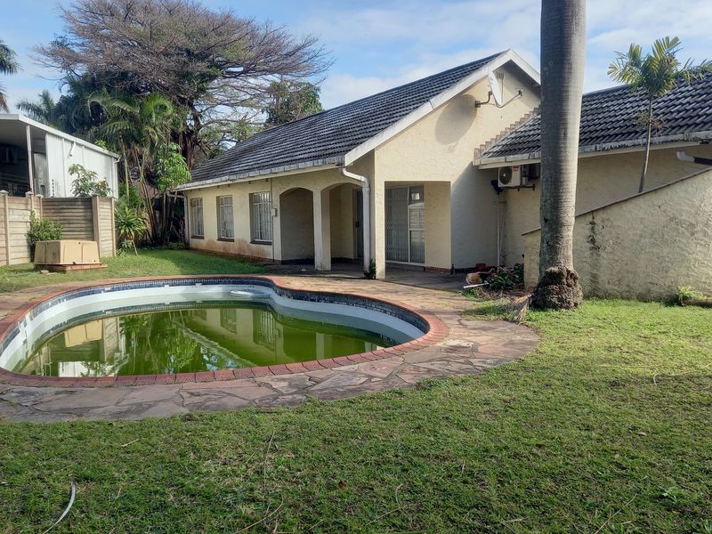 Rear view of the property featuring a swimming pool, paved surround, and a tiled roof structure with exterior wall access.
