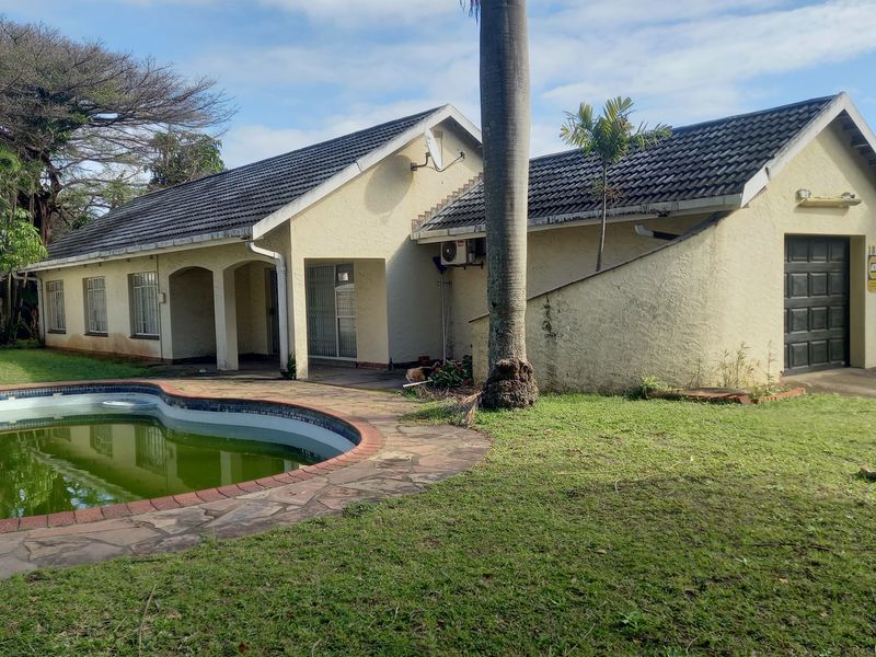 Rear view of the property featuring a swimming pool, paved patio area, and access to the garage, set within a large garden.