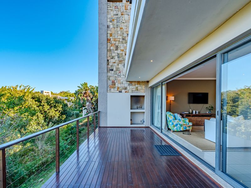 Spacious covered balcony featuring timber decking, stone cladding, and a built-in braai, seamlessly connecting to the interior living area through large sliding glass doors.