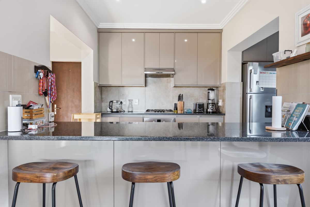 Modern kitchen featuring sleek high-gloss cabinetry, a dark granite breakfast bar, gas hob, and integrated appliances with a clean, contemporary finish.