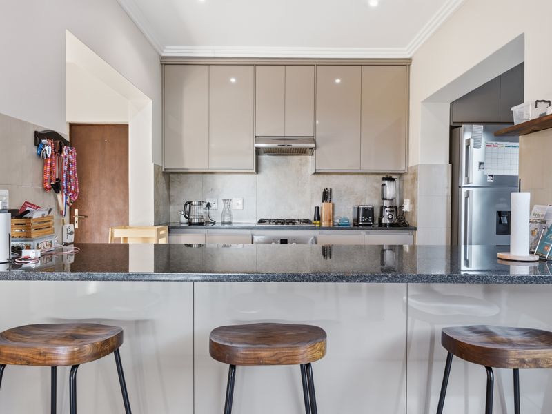 Modern kitchen featuring sleek high-gloss cabinetry, a dark granite breakfast bar, gas hob, and integrated appliances with a clean, contemporary finish.