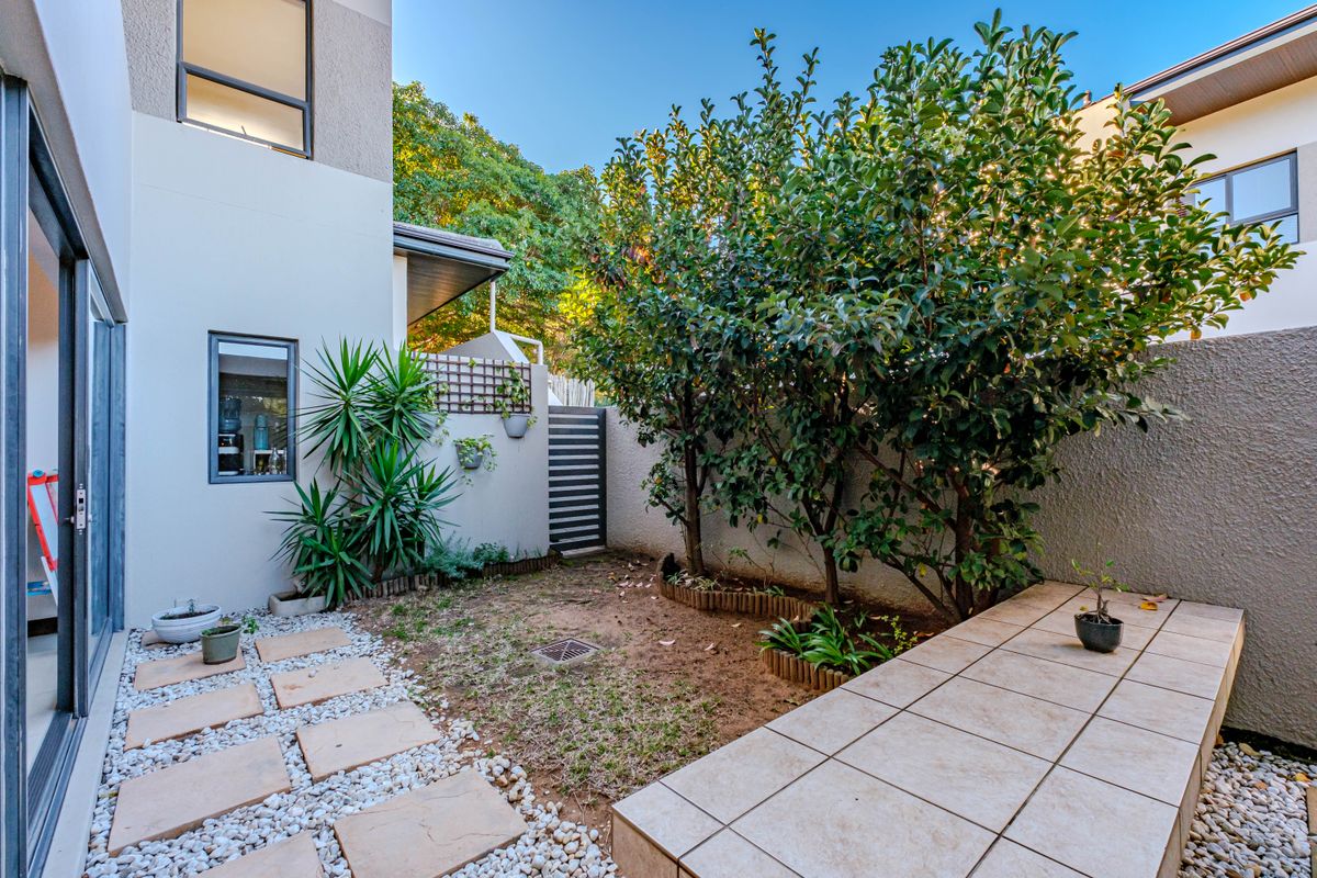 A private rear courtyard featuring a tiled patio area, pebble landscaping, and established trees, accessible via large sliding glass doors.