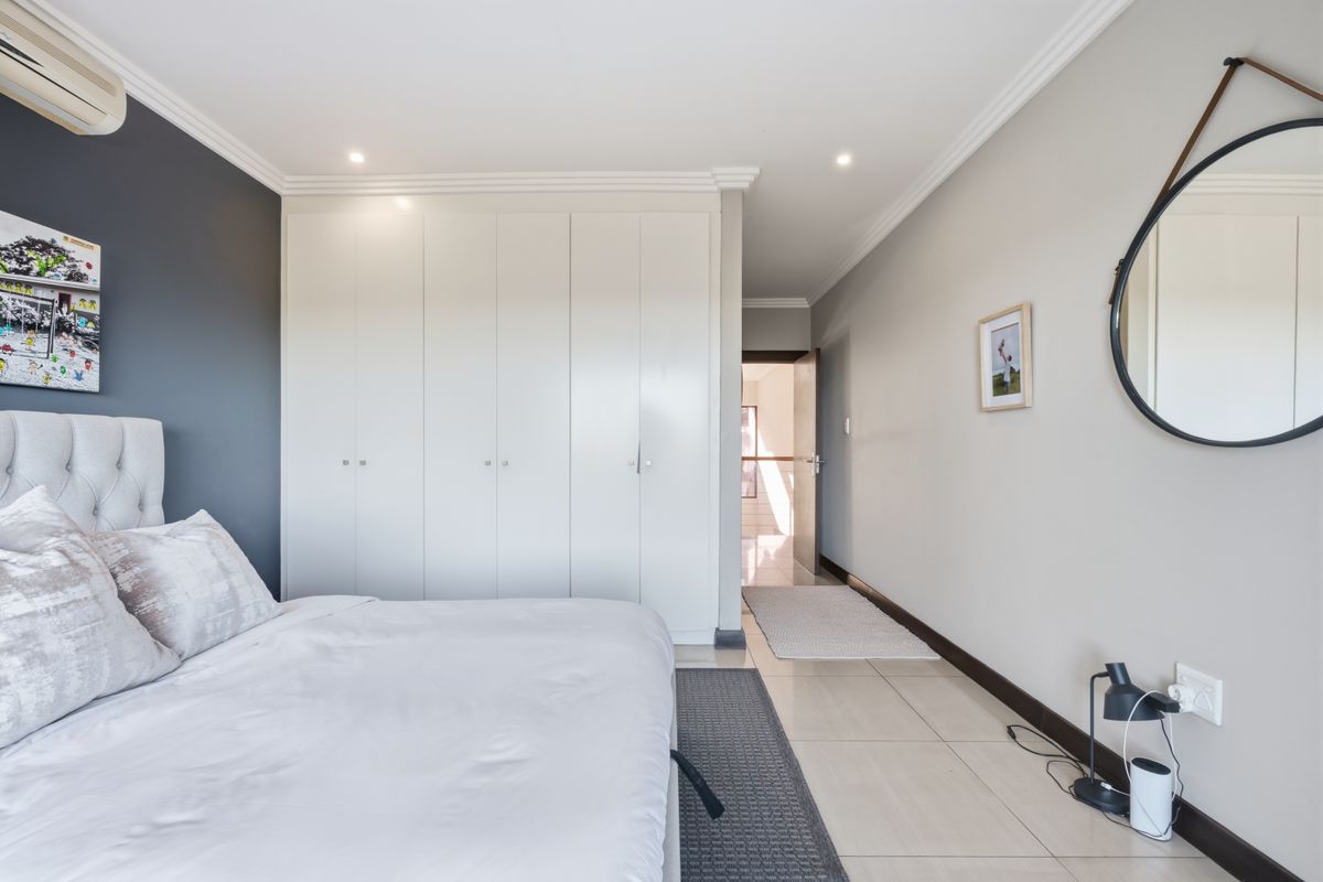 A well-maintained bedroom featuring built-in cupboards, crown molding, recessed lighting, and neutral tiled flooring with a modern accent wall.