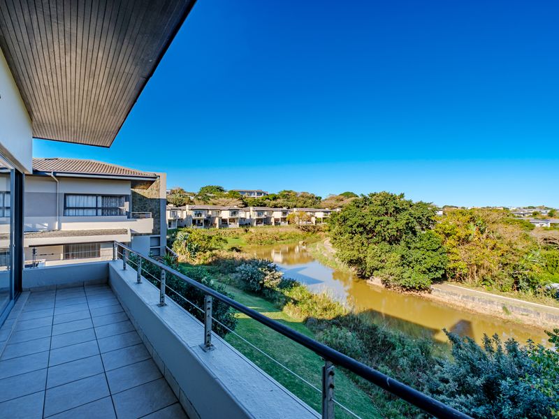 A spacious covered balcony featuring tiled flooring and a stainless steel balustrade, offering scenic views over the river and surrounding estate landscape.