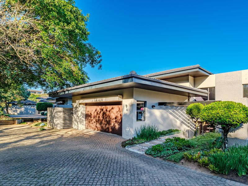 Front exterior view of the property featuring a paved driveway, integrated garage, and well-maintained landscaped garden under a clear blue sky.