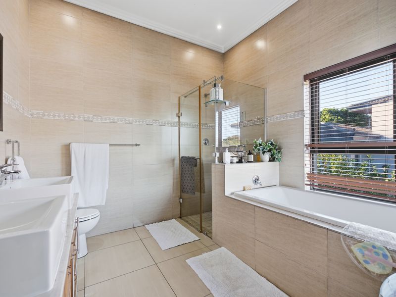 Modern bathroom featuring a double vanity, a glass-enclosed shower, and a built-in bathtub with neutral floor-to-ceiling tiling.