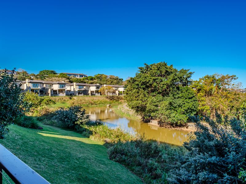 A scenic view overlooking a tranquil pond, lush green lawns, and mature trees, with residential properties visible in the background.
