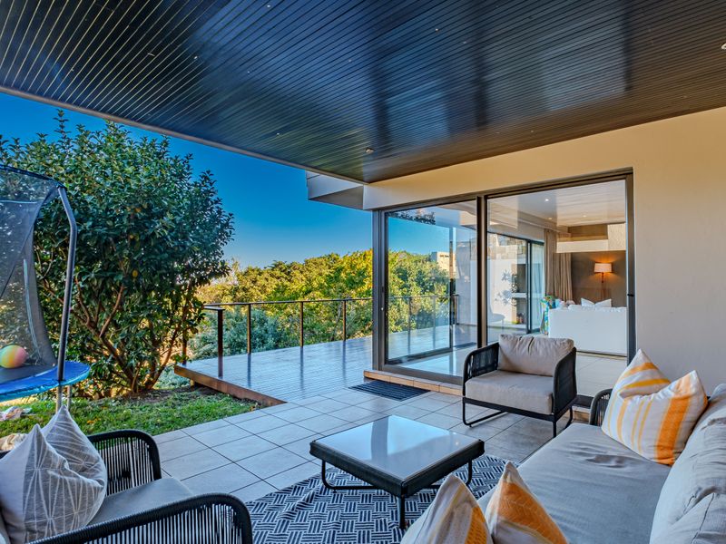 A spacious covered patio featuring tiled flooring, a timber-look ceiling with recessed lighting, and seamless access to an adjoining timber deck and interior living space.