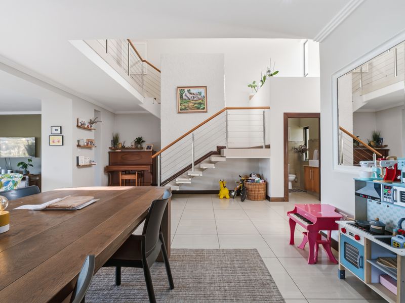 Spacious open-plan living area featuring a modern staircase with stainless steel balustrades, neutral tiled flooring, and high ceilings.