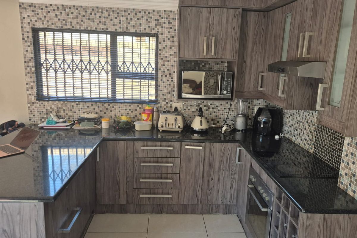 A functional kitchen featuring wood-grain cabinetry, granite countertops, a mosaic tile backsplash, and integrated appliances including an oven and hob.