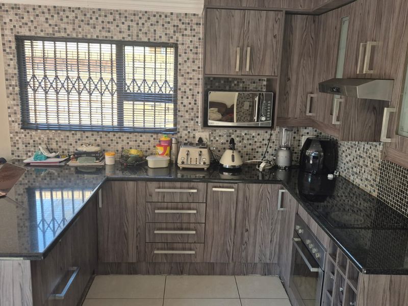 A functional kitchen featuring wood-grain cabinetry, granite countertops, a mosaic tile backsplash, and integrated appliances including an oven and hob.
