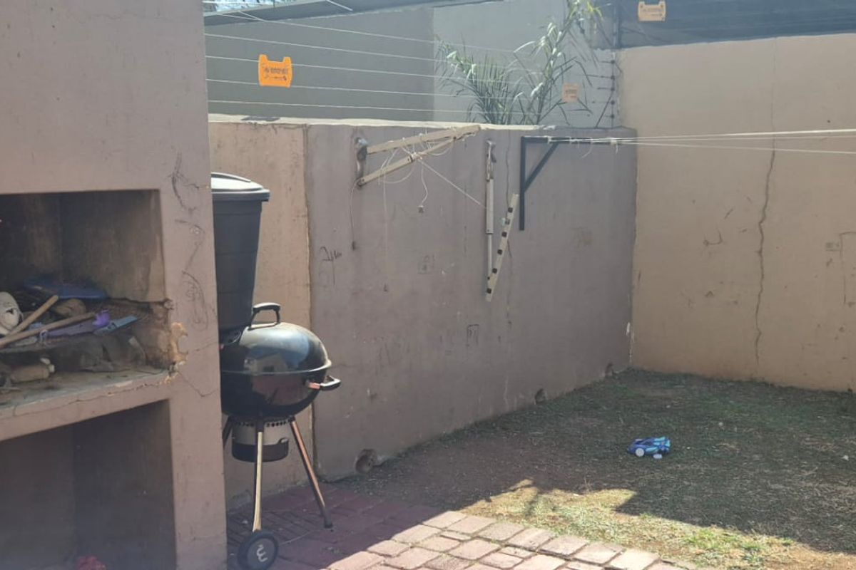 Rear courtyard area featuring a built-in braai, paved patio space, and perimeter wall with electric fencing.