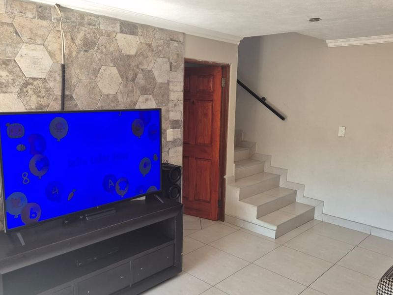 Living room featuring a stone-clad accent wall, tiled flooring, and an internal staircase with a handrail.