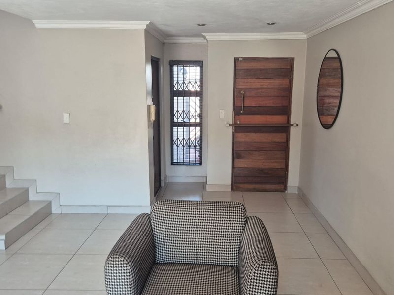 Entrance hall featuring tiled flooring, a solid wooden front door with security gate, and a staircase leading to the upper level.