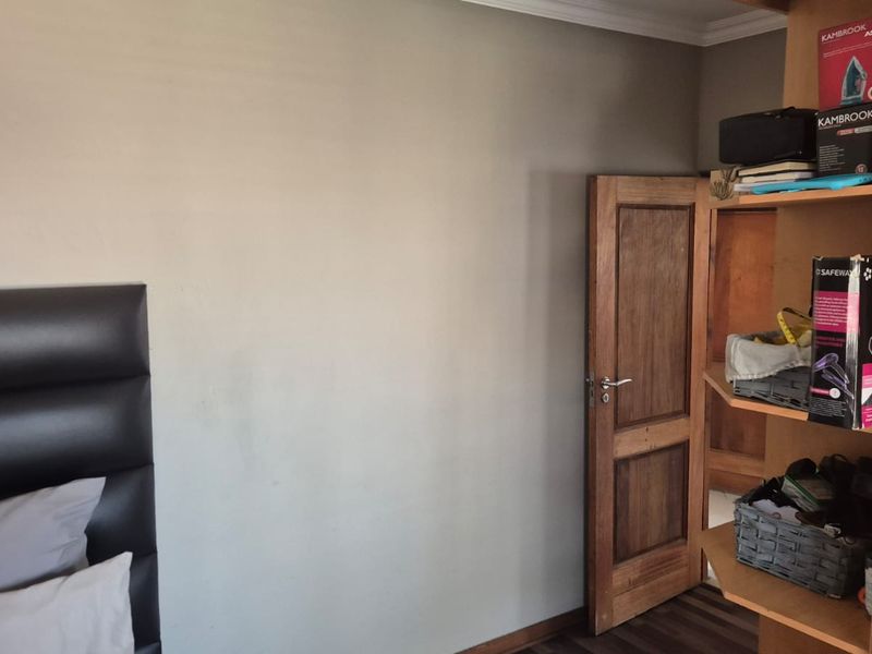 A bedroom featuring laminate flooring, a wooden door, and crown molding, providing a neutral base for interior design updates.