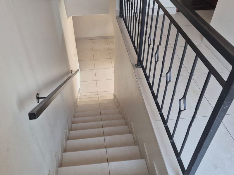 A clean, tiled staircase featuring a modern black metal balustrade and a matching wall-mounted handrail, providing a functional transition between levels.