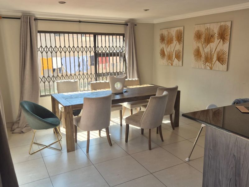 Open-plan dining area featuring neutral tiled flooring, recessed lighting, and a seamless transition to a modern kitchen with granite countertops.