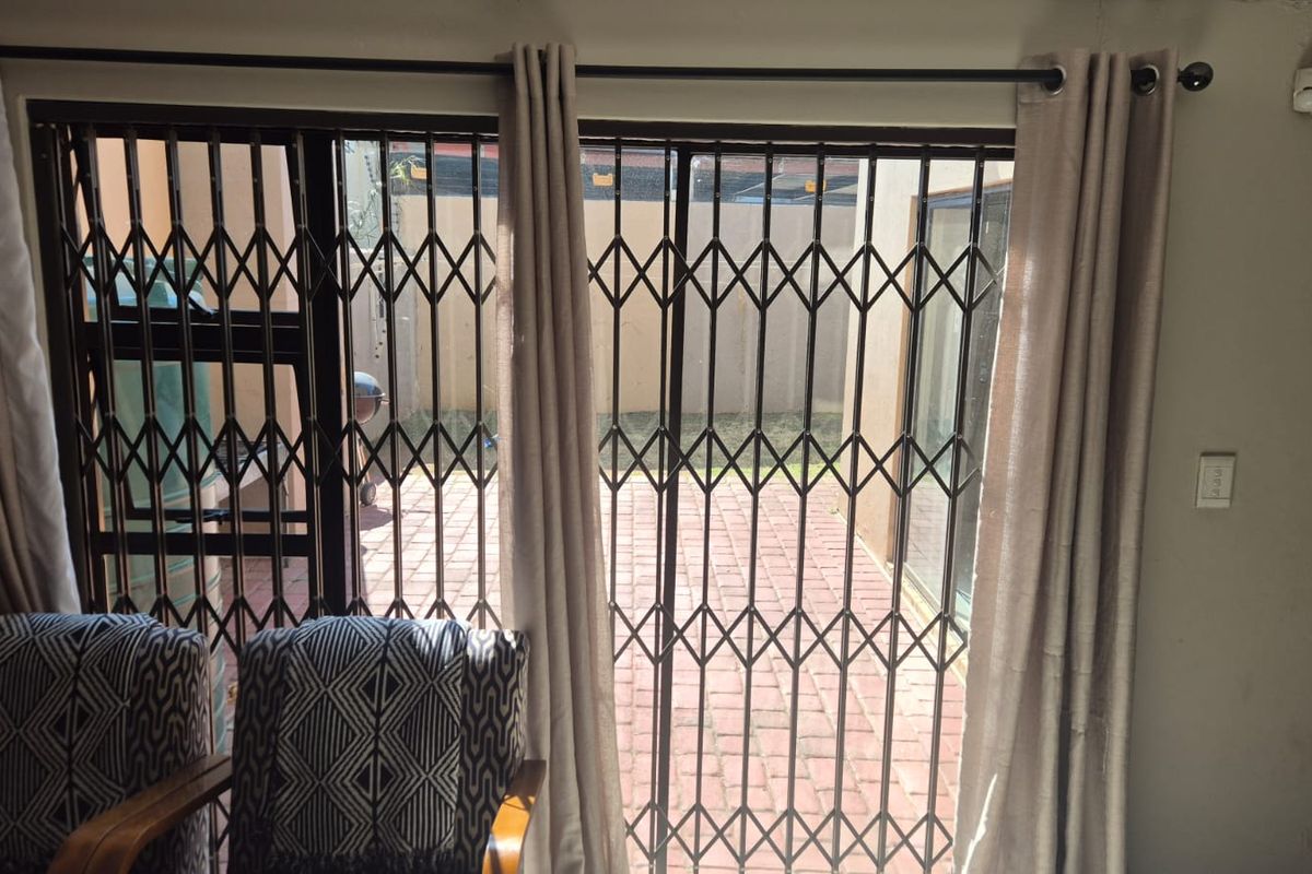 Living area featuring a sliding glass door with a security gate, providing direct access to an outdoor brick-paved patio space.