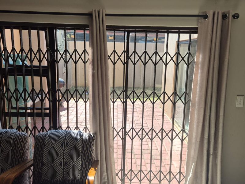 Living area featuring a sliding glass door with a security gate, providing direct access to an outdoor brick-paved patio space.